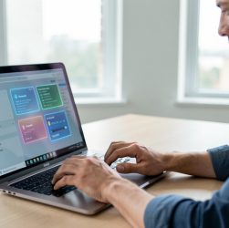 Un homme analyse des services numériques sur un ordinateur portable dans un bureau moderne et lumineux.